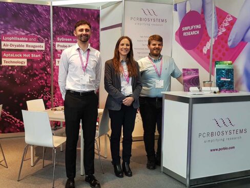 PCR Biosystems' booth at Analytica. 3 people, 1 women and 2 men stand infront of it.